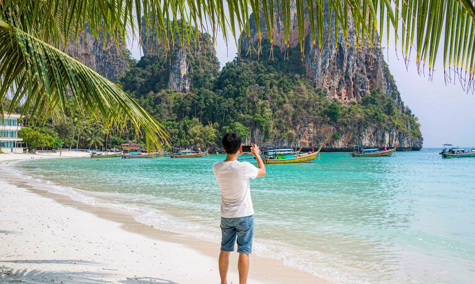 普吉島海灘上使用 eSIM 的旅客,長尾船與石灰岩峭壁是典型海島場景